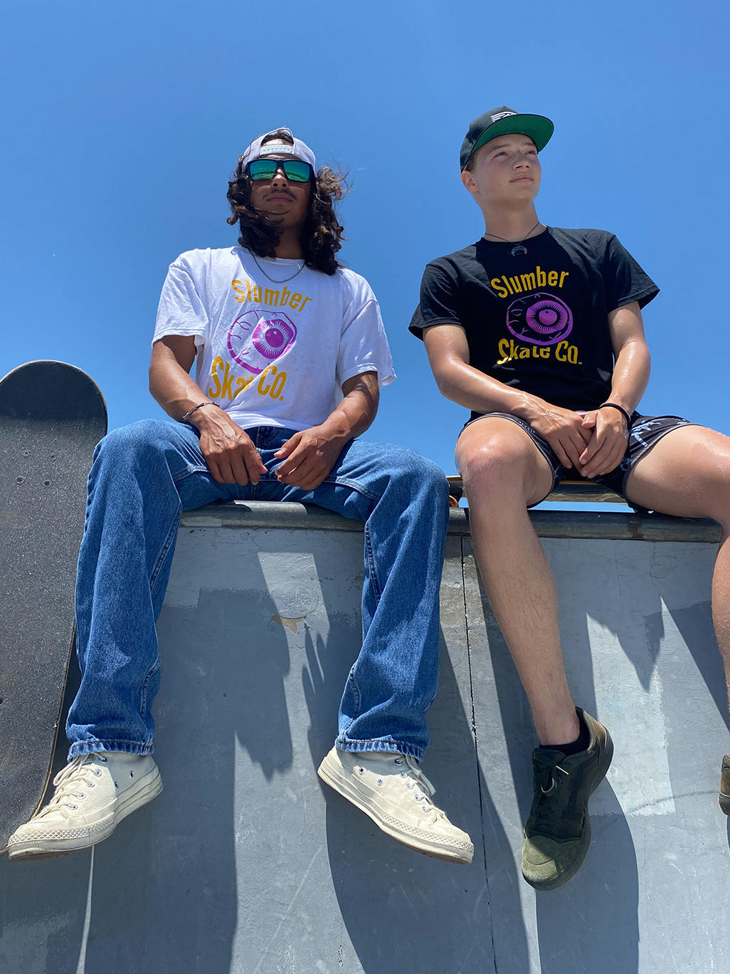 two young skateboarders sitting on edge of bowl looking away