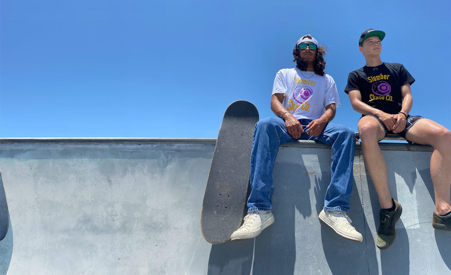 two young skateboarders sitting on edge of bowl looking away